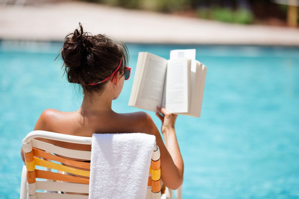 Une jeune femme qui lit un livre au bord de la piscine 